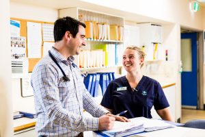 A medium close up shot of a male doctor and female nurse smiling at each other while filling out paper work.
