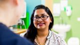 A close up over the shoulder photo of a female wearing glasses smiling at the person she is talking to.