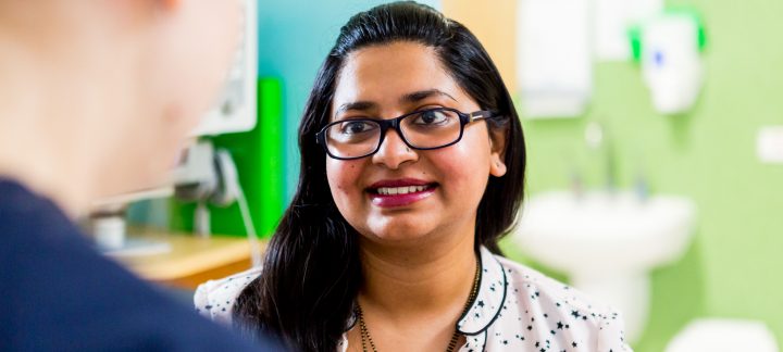 A close up over the shoulder photo of a female wearing glasses smiling at the person she is talking to.