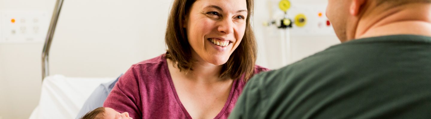 An over the shoulder photo of a woman smiling at a man while holding a baby.