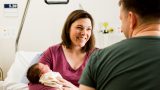 An over the shoulder photo of a woman smiling at a man while holding a baby.