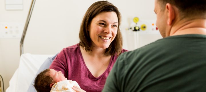 An over the shoulder photo of a woman smiling at a man while holding a baby.