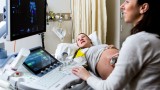 A pregnant woman and an ultrasound technician smile at the screen during an ultrasound.