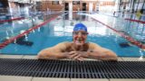 95-year-old Mercy Health Home Care client Father Chris Baker, enjoying swimming in a pool with his arms leaning up whilst smiling at camera.